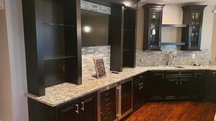 Stone basement bar with sink, cabinets, and tv.