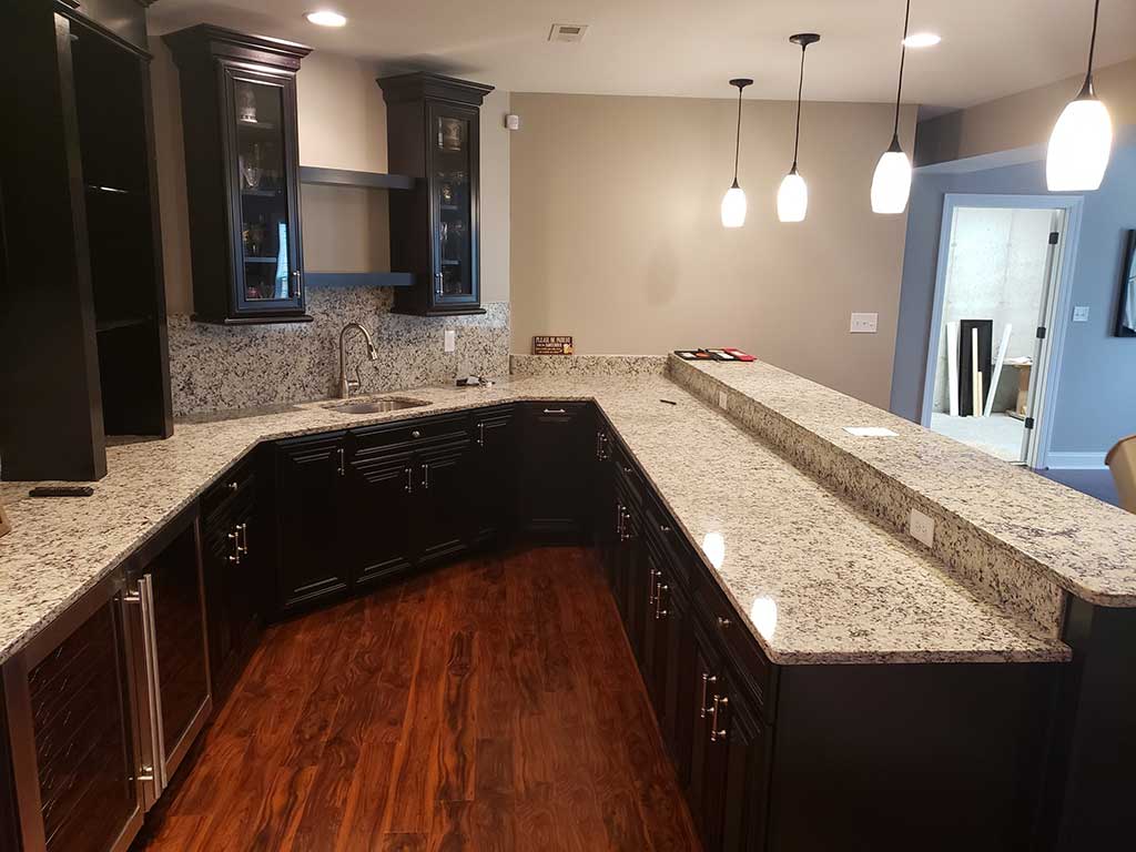 Stone basement bar with sink, cabinets, and tv.