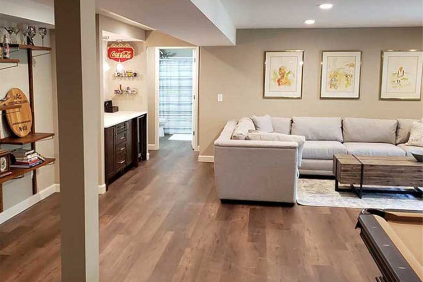 Finished basement with tan walls, couch, small bar area, and bathroom