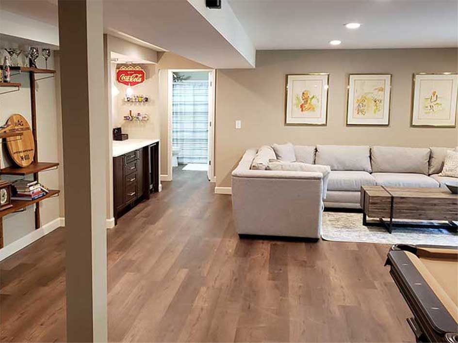 Finished basement with tan walls, couch, small bar area, and bathroom